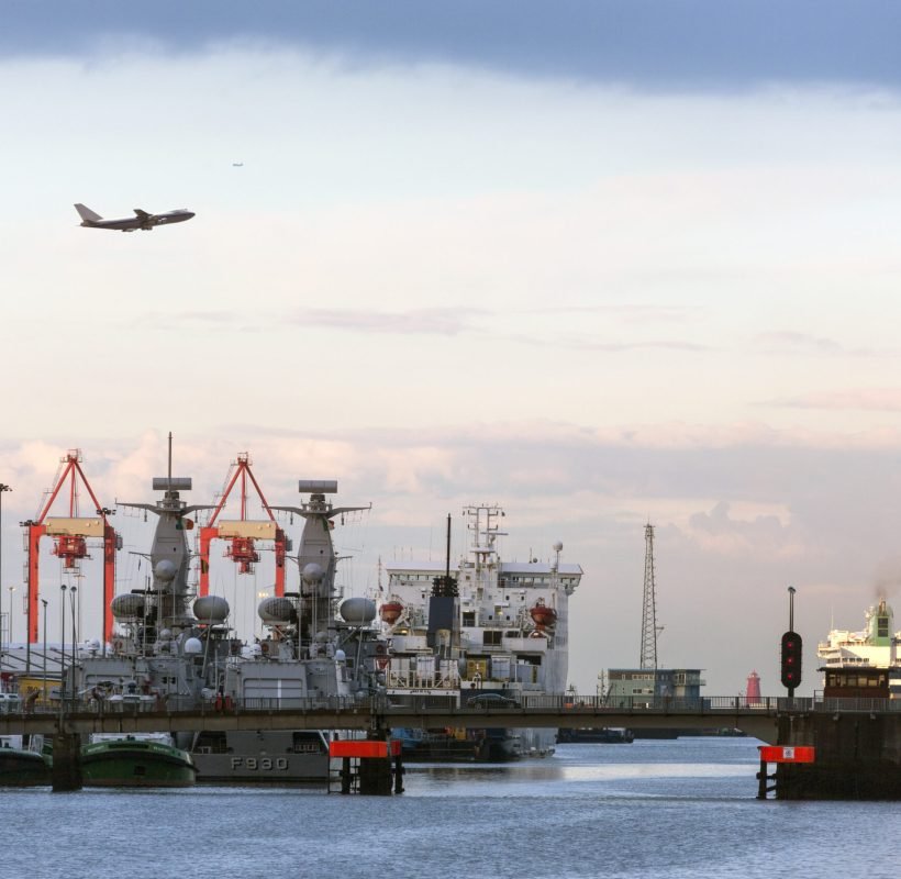 Aircraft flying over the port of Dublin – Ireland A jet airliner flying over the ships in the port of Dublin in the late evening light -  Republic of Ireland.